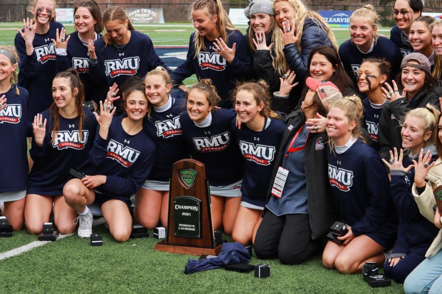 Womens lacrosse crowds around their MAC championship trophy. Photo Credit: Ethan Morrison